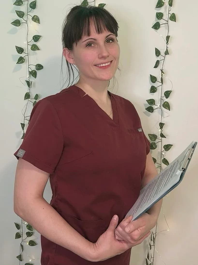 Osteopath in burgundy scrubs holding a patient intake clipboard in her Mississauga clinic
